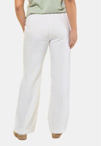Vita linnebyxor med breda ben och hög midja, lätt textur och något gatherad bak, i kombination med tan-färgade kilklackar.