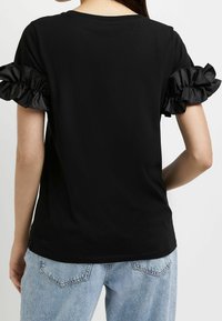 Camiseta negra con mangas cortas de satén con volantes, diseño ajustado y escote redondo, combinada con jeans de mezclilla azul claro.