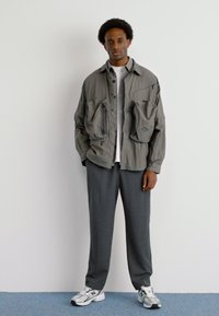 Gray oversized jacket with front pockets, paired with gray trousers and white sneakers featuring black accents. Simple, utilitarian design.