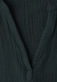 Tissu texturé vert foncé avec un col en V profond et des surpiqûres visibles le long des bords.