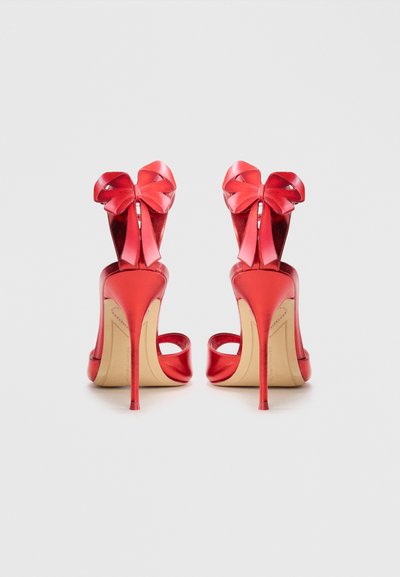 Pantofi roșii cu toc înalt, cu un finisaj patent lucios, vârful deschis și un accent mare sub formă de fundă pe toc. Design stiletto cu o formă subțire.