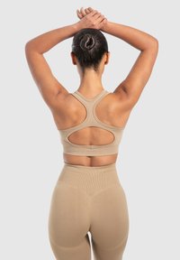 Beige urheiluliivi, jossa on pyöreä selkä, leikattu yksityiskohtia ja paksut hihnat, yhdistetty korkeavyötäröisiin yhteensopiviin leggingseihin, joissa on ribbitekstuuri.