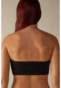 Musta olkaimeton bandeau-toppi, joka on valmistettu sileästä joustavasta kankaasta. Se on yksinkertainen muotoilu, joka kiertää tiukasti vartalon ympärille.