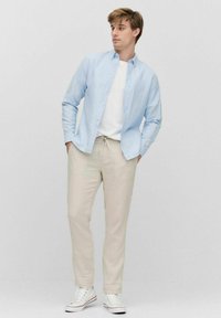 Lichtblauw overhemd met knopen over een wit T-shirt, gecombineerd met beige linnen broek en witte sneakers. Eenvoudig, casual ontwerp met neutrale kleuren.