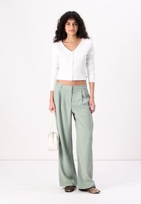 Haut blanc à rayures avec des boutons et des manches longues, associé à un pantalon large taille haute vert menthe et des ballerines à imprimé animal. Sac à main blanc.