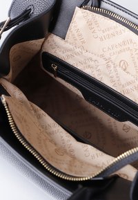 Interno di una borsa a tracolla grigia con una fodera beige, caratterizzato da motivi a logo stampati e una tasca con zip. Finiture della cerniera in tono oro.
