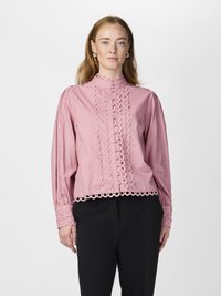Pink blouse with a high neck, lace trim, and buttoned front. Features puffed sleeves and circular cutout accents along hems and cuffs.