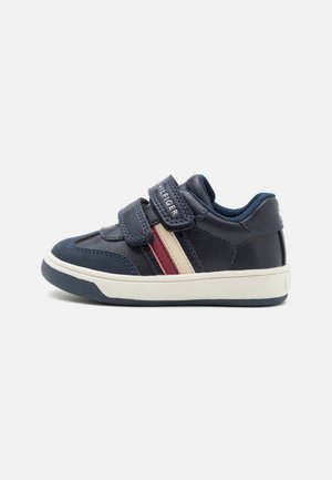 Granatowe skórzane sneakersy z dwiema zapięciami na rzepy, z czerwonymi i kremowymi paskami po bokach, białą podeszwą i teksturowanym wierzchem.