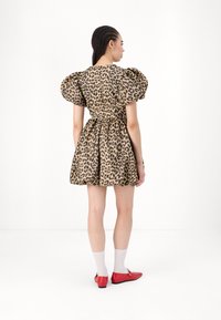 Leopard print dress with puffed sleeves, fitted waist, and flared skirt. Worn with red shoes and white socks, featuring textured fabric.