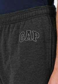 Pantalones de chándal grises hechos de una tela suave, con cintura elástica, bolsillos laterales y un prominente logo "GAP" en letras oscuras.