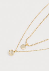 Collana a strati in oro con pendente rotondo in pietra trasparente, ciondolo circolare liscio e catena fine con accenti di perline.