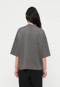 Γκρι τοπ με κοντά μανίκια και ψηλό λαιμό. Άνετη ε φαρμογή, λεία υφή και χαμηλωμένοι ώμοι. Απλός σχεδιασμός, ελάχιστες λεπτομέρειες και χωρίς σχέδια.