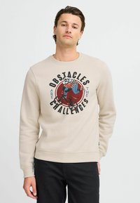 Beige sweatshirt with a round graphic featuring a panda on a bike and text "Obstacles are the Challenges." Ribbed cuffs and hem.