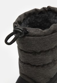 Botte isolée noire avec un dessus en tissu matelassé et texturé, équipée d'un système de fermeture à cordon, conçue pour la chaleur et le confort.