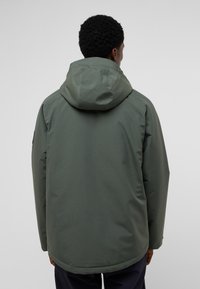 Green waterproof jacket with a hood, featuring a smooth texture and a straight cut. Includes a logo patch on the shoulder.