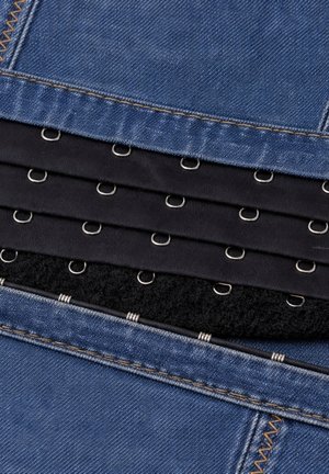 Primo piano di tessuto denim stratificato con strisce di tessuto nero che presentano chiusure metalliche a gancio e occhiello allineate in file.