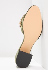 Vihreät samettitossut, joissa on musta kumipohja, koristekivillä sivuilla ja pyöreä kärki. Kultaiseen ompeluun pohjassa.