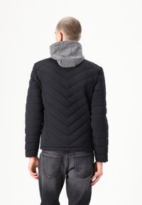 Jachetă puffer neagră cu model în zigzag și căptușeală gri la glugă. Dispune de mâneci lungi și o croială structurantă. Purtați-o peste pantaloni din denim închisi la culoare.