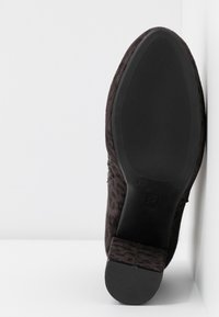 Chaussure en daim noir avec un motif léopard texturé, un talon bas et une semelle en caoutchouc. Couture visible et design à bout arrondi.