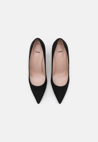 Escarpins en daim noir à bout pointu. L'intérieur présente une doublure lisse de couleur beige clair et un logo discret.