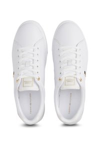 Paire de baskets blanches basses avec lacets blancs, œillets dorés et marquage "Tommy Hilfiger" sur la languette et la semelle intérieure visibles depuis le dessus.