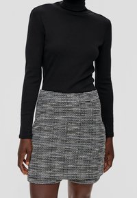 Svart långärmad polotröja i kombination med en åtsittande minikjol med ett texturerat svart och vitt randigt mönster.