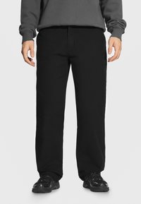 Czarne bawełniane spodnie o prostym kroju, z płaskim przodem, kieszeniami po bokach i gładką fakturą. W połączeniu z czarnymi trampkami.