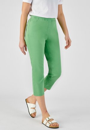 Pantaloni cropped verdi realizzati in un tessuto morbido con vita aderente e due tasche laterali, abbinati a sandali bianchi con doppia fibbia.