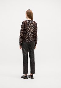 Pull en motif léopard marron et noir, associé à un pantalon texturé foncé. Les chaussures affichent une finition noire brillante avec des accents dorés.