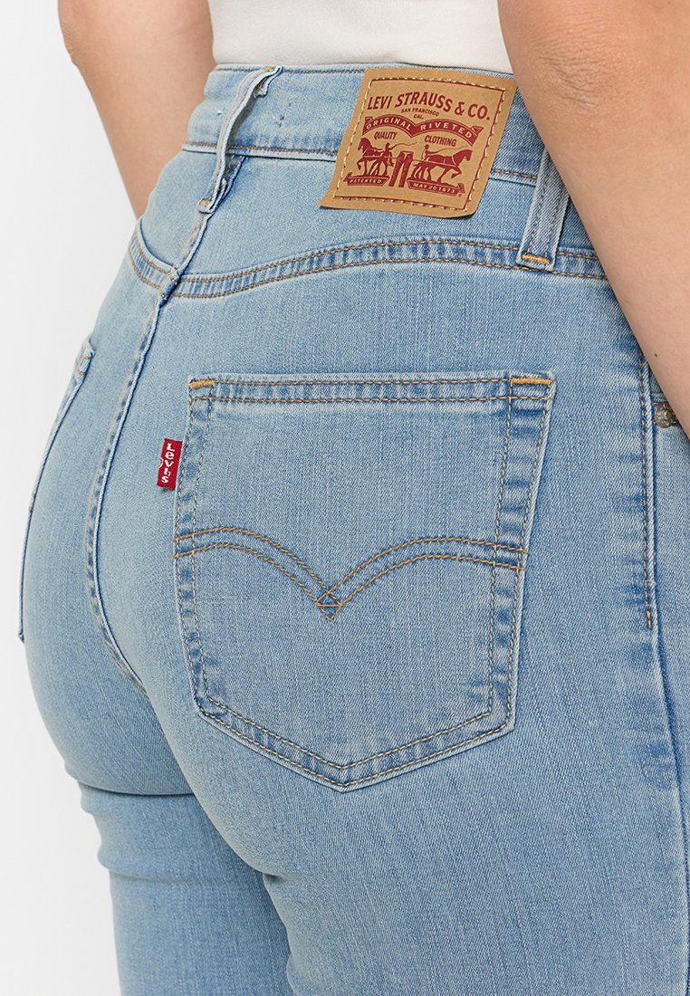 Detalle de una persona que lleva puestos unos vaqueros Levi's de color azul claro, destacando el bolsillo trasero, la etiqueta roja de Levi's y el parche de cuero de la marca en la cintura.