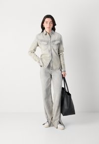 Giacca in denim grigia chiara con tasche frontali, abbinata a pantaloni a gamba larga dello stesso colore. Una borsa tote in pelle nera e scarpe da ginnastica bianche completano il look.
