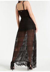 Schwarzes Häkelkleid mit tailliertem Oberteil und einem langen, durchsichtigen Rock, der offene Muster und Fransen am Saum aufweist.