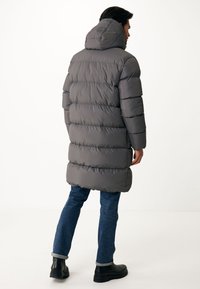 Abrigo acolchado gris con costuras horizontales, capucha y largo hasta la mitad del muslo. Combinado con jeans azules y botas negras, diseño minimalista.