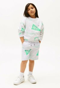 Grijze katoenen sweatshirt met groene geometrische patronen, gecombineerd met bijpassende shorts. Witte sneakers en crew-sokken maken de outfit compleet.