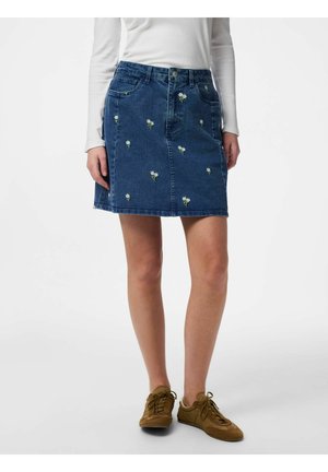 Modrá rifľová sukňa s malou bielou kvetinovou výšivkou, nosená s bielym topom s dlhým rukávom a hnedými šnurovacími topánkami.