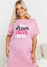 Kort rosa nattlinne i mjukt tyg med en stor textdesign som säger "drömmen börjar här" i olika färger och hjärtaccenter.