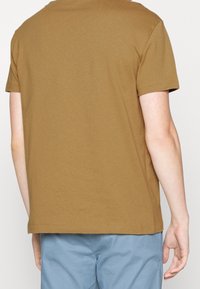 Hnědá bavlněná tričko s uvolněným střihem, krátkým rukávem a kulatým výstřihem. Hladká textura s jednoduchým, jednobarevným designem.