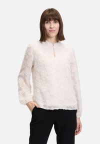 Helles rosa Bluse mit strukturierten Blumenmustern, rundem Ausschnitt und langen Ärmeln. Abgeschlossen mit einem geraden Saum und einer kleinen Schlüssellochöffnung vorne.