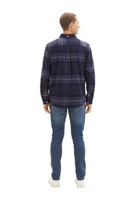 Granatowa koszula w kratę z flaneli z zapięciem na guziki, długimi rękawami i luźnym krojem, w zestawie z jasnoniebieskimi dżinsami i białymi trampkami.