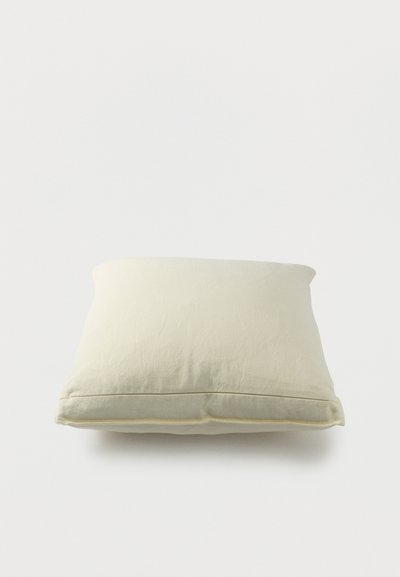 Coussin rectangulaire crème doux avec tissu lisse et légères rides, posé sur un fond blanc uni.
