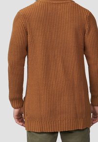 Långärmad, stickad tröja i en varm brun färg med ett strukturerat mönster och ribbade ärmslut och nederkant. Visar en avslappnad passform.