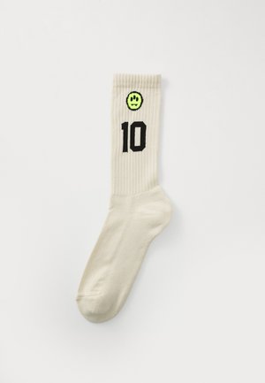 Calzini a coste color crema con un "10" nero e una faccina sorridente verde sul risvolto. Tessuto morbido e elastico.