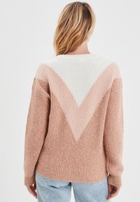Maglione a coste con un design a blocchi di colore a forma di V; presenta tonalità di rosa chiaro, crema e beige morbido; texture morbida e vestibilità rilassata.