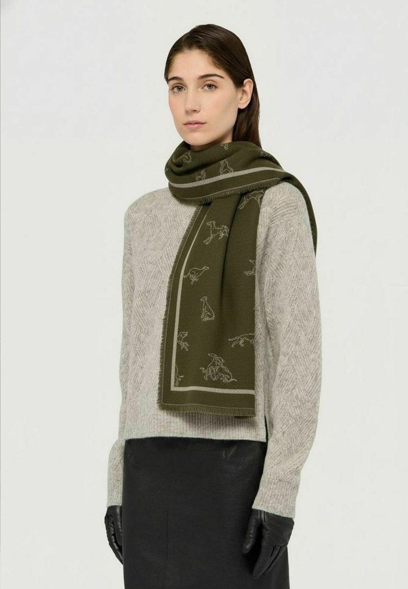 Sciarpa verde oliva con motivi animali e bordo a contrasto, indossata sopra un maglione lavorato a maglia grigio chiaro, abbinata a una gonna in pelle nera e guanti.