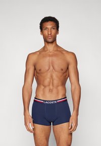 Blaue Boxershorts mit einem markenbezogenen Bund, der rot-weiße Streifen aufweist. Weicher Baumwollstoff mit einer figurnahen Passform.