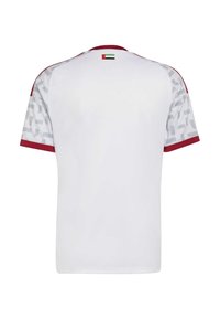 Maglietta sportiva bianca con accenti rossi, maniche corte e un motivo geometrico grigio. Dettaglio bandiera sul colletto. Tessuto dalla texture liscia.