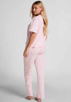 Lichtroze pyjamaset met een gestippeld patroon en rode hartjes; losvallend shirt met korte mouwen en broek met rechte pijpen. Zachte stoftextuur.