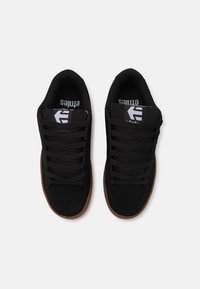 Schwarze Sportschuhe mit einem Obermaterial aus Wildleder und Stoff, runder Zehenform, flachen Schnürsenkeln und einer Gummisohle in kontrastierendem Braun.