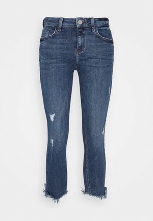 Jean skinny bleu foncé avec des détails usés et des ourlets effilochés, équipé de poches avant et d'une fermeture à bouton.