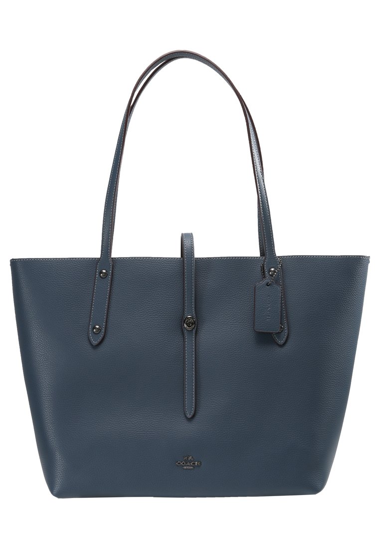 Bolso tote de cuero azul con textura suave, dos asas largas y cierre a presión. Presenta un logotipo y una etiqueta adjunta. Forma rectangular.